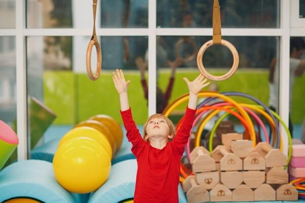Kleiner Junge, der sich nach Ringen streckt, die von der Decke herab h&auml;ngen