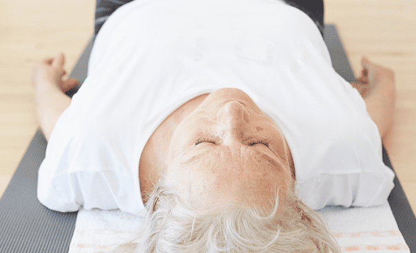 Seniorin liegt entspannt auf Yogamatte beim Präventionskurs für Entspannung